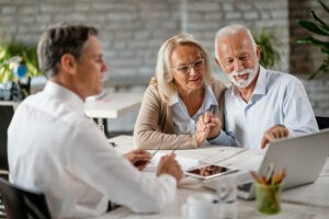 happy-senior-couple-holding-hands-using-laptop-while-having-meeting-with-financial-advisor-office-senior-man-is-pointing-something-laptop