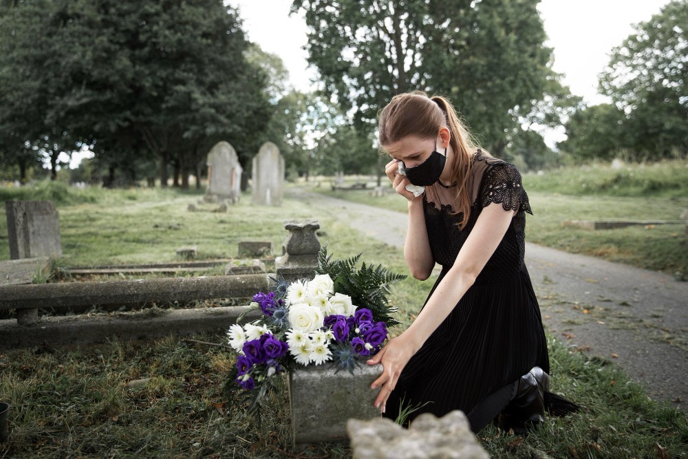 Grieving woman at loved one’s grave, symbolizing emotional and legal challenges of collecting debts after death.